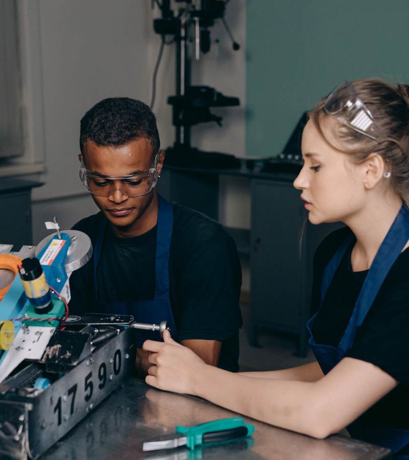 Deux apprentis en blouse de travail et lunettes de protection étudiant un équipement technique en atelier