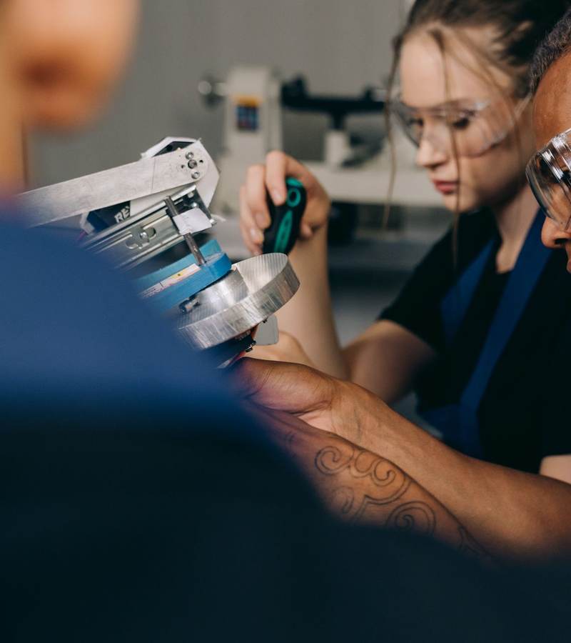 Apprentis équipés de lunettes de protection manipulant une pièce mécanique en atelier de formation