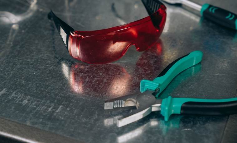 Lunettes de protection rouges et pinces d’électricien posées sur une surface métallique