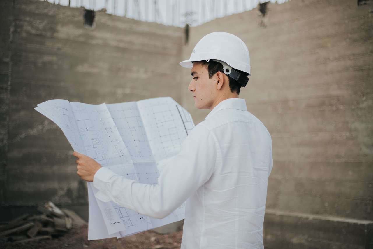 Technicien en casque blanc et chemise claire consultant un grand plan sur un chantier